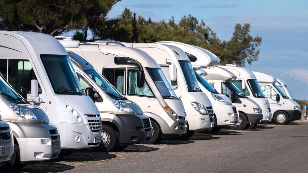 A line of white and gray RVs sitting in an RV rental lot