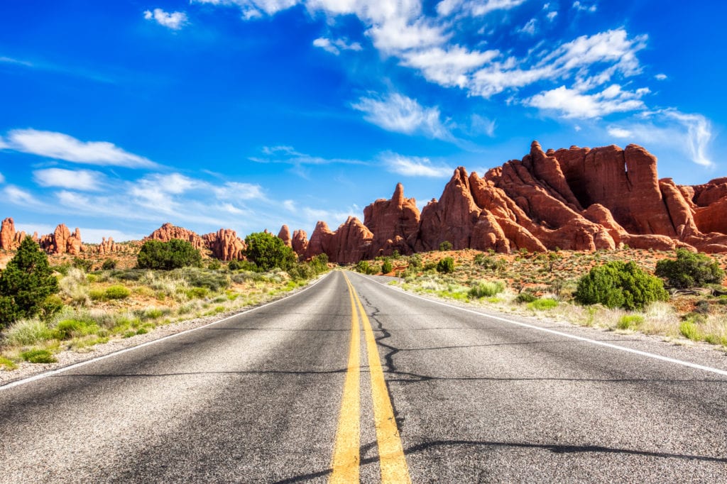 Driving through the-Desert with Monument Rock along the Road During Sunny Day, Arches NP Driving through the Desert with Monument Rock along the Road During Sunny Day Arches NP from Tumbleweed Travel