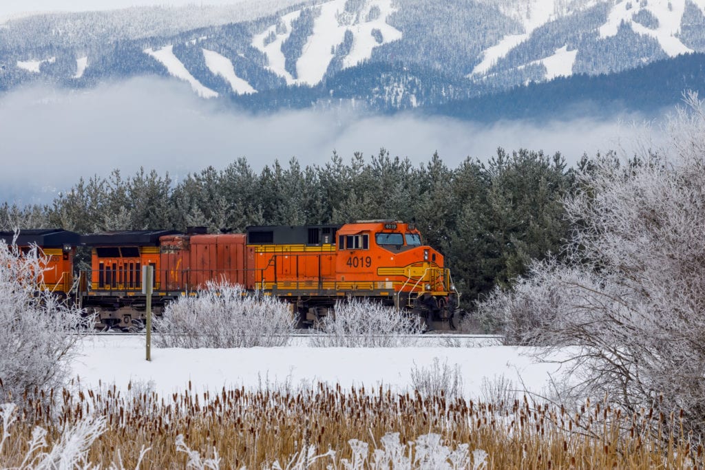 locomotive pulling train in winter close to Whitefish Montana with Whitefish ski resort in background from Tumbleweed Travel